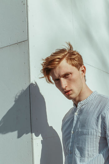 PORTRAIT OF YOUNG MAN LOOKING AWAY WHILE STANDING ON WALL