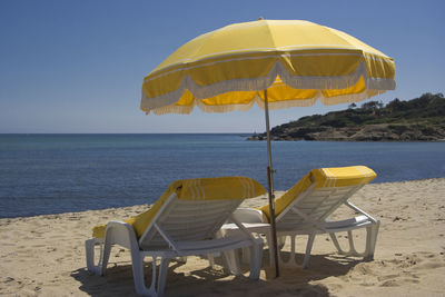 Deck chairs on beach against clear blue sky