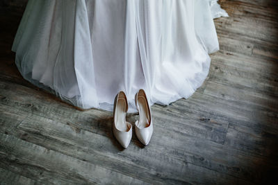 A pair of beige shoes stand near the bride's dress on the floor