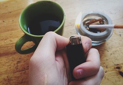 Cropped hand holding lit cigarette lighter on wooden table