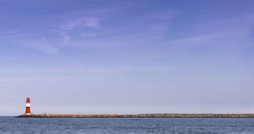 Lighthouse by sea against blue sky