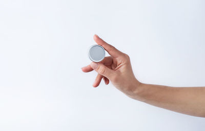 Woman hand holding blank round tin container for lip balm or cream on light gray background