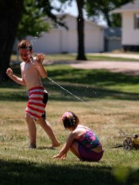 Water spraying on shirtless boy with sister in yard