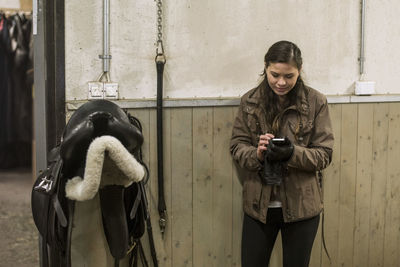 Young woman using smart phone in horse stable