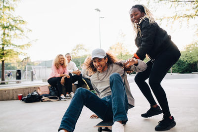 Teenage girl pushing happy man on skateboard while playing at park