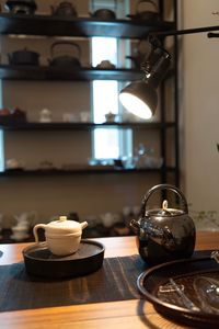 Close-up of illuminated electric lamp over teapots on table at home