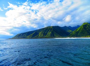 Scenic view of sea by mountain against sky