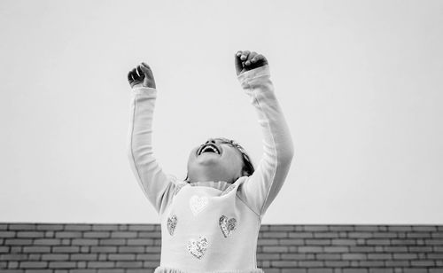 Rear view of woman with arms raised standing against wall