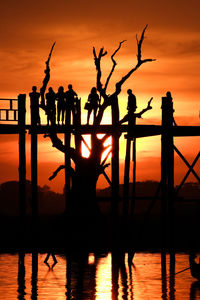 Silhouette people on footbridge against sky during sunset