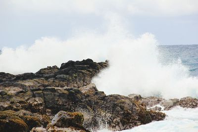 Waves splashing on rocks in sea against sky