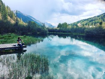 Man sitting by lake against sky