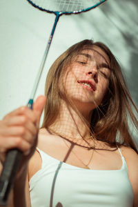 Beautiful young woman holding badminton racket against wall