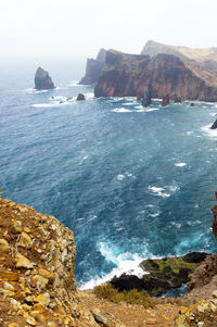 High angle view of rocky coastal feature against clouds