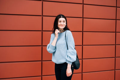 Portrait of smiling young woman standing against brick wall