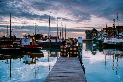 Boats moored in harbor at sunset