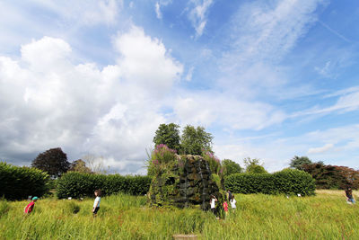 People on grassy field against cloudy sky