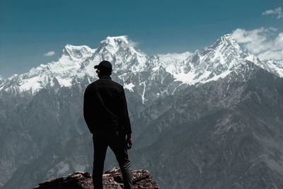 Rear view of man standing on rock against snowcapped mountains