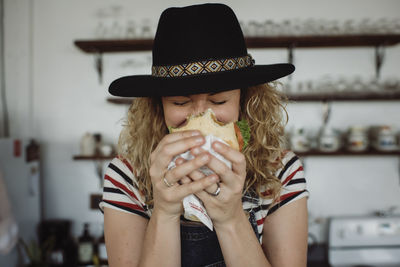 Close-up of woman wearing hat holding sandwich while standing at home
