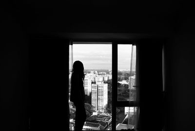 Silhouette woman standing by window in city