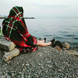 Low section of person sitting on pebbles at sea shore