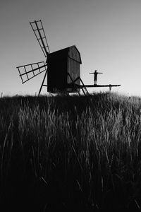 Silhouette person with arms outstretched standing on traditional windmill against clear sky during sunset