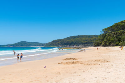 People on beach against clear blue sky