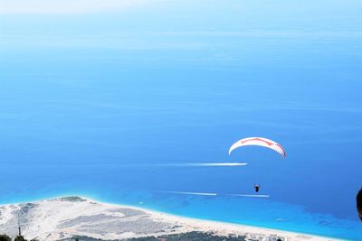 Person paragliding over sea against blue sky