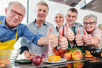 Portrait of smiling people showing thumbs up in kitchen