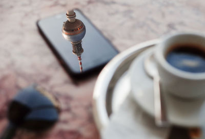 Reflection of television tower on mobile phone on a coffee table of pink   marble with espresso cup 