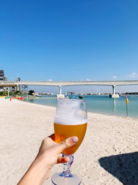 Midsection of woman holding drink at beach against sky