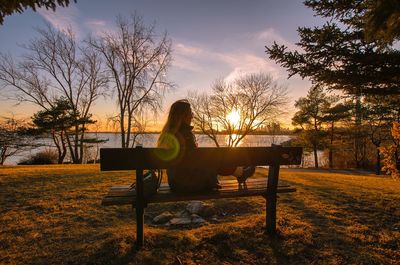 Silhouette man sitting on bench in park during sunset
