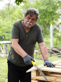 Portrait of man working on wood against trees