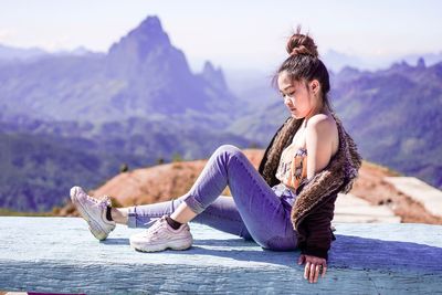 Beautiful young woman sitting on wood against mountains