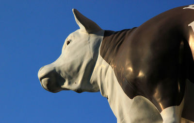 Low angle view of cow statue against clear blue sky