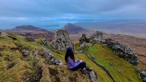 Rear view of woman sitting on landscape against sky