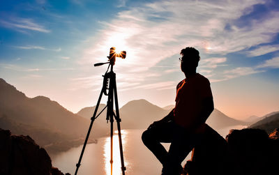 Silhouette man photographing against sky during sunset