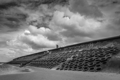 Groynes by wall at sandy beach against cloudy sky