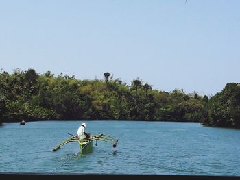 Man sitting on boat sailing in river against clear sky