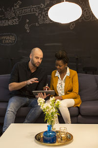Coworkers using digital tablet on sofa