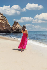 Rear view of woman standing at beach against sky