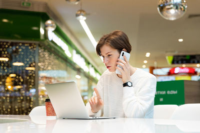 Young woman using mobile phone while sitting on table