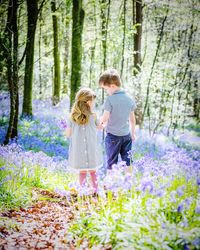 Girl standing by flowering plants and trees in forest