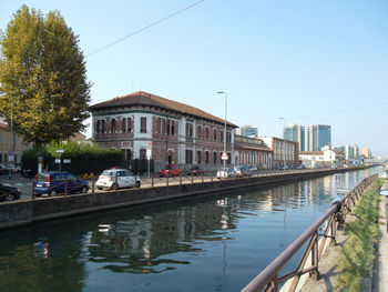 Canal by buildings in city against clear sky