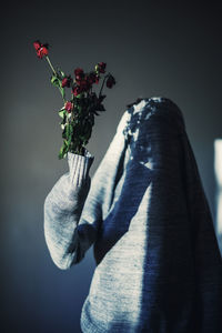 Person holding wilted flowers with covered face against wall