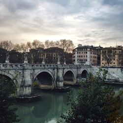 Arch bridge over river by buildings against sky