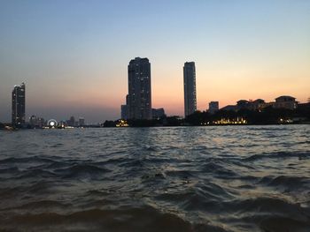 Sea by buildings against clear sky at sunset