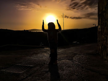 Rear view of silhouette person standing on street during sunset