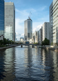 Modern buildings by river against sky in city