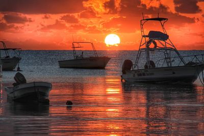 Boats moored in sea against orange sky during sunset