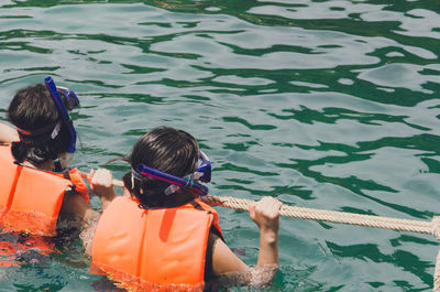 Rear view of people holding rope while snorkeling in sea